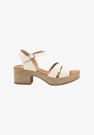 Sandalias de tacón blancas de cuero con dos correas cruzadas, correa en el tobillo ajustable y un tacón de bloque de madera texturizada. Plantilla interior de un suave color marrón.