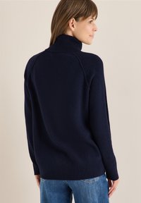 Pull à col roulé navy avec une coupe décontractée, des poignets et un ourlet côtelés. Texture douce avec des manches raglan et sans motifs ni accents visibles.