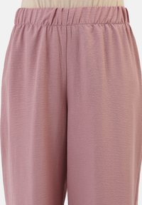Lichtroze, zacht aanvoelende elastische taillebandbroek met een relaxte pasvorm en subtiel crêpe-achtig patroon, zichtbare stiksels en zonder zakken.