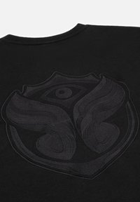 Zwarte t-shirt met een gestructureerd zwart geborduurd logo op de achterkant, met een schildvorm en vloeiende ontwerpelementen.