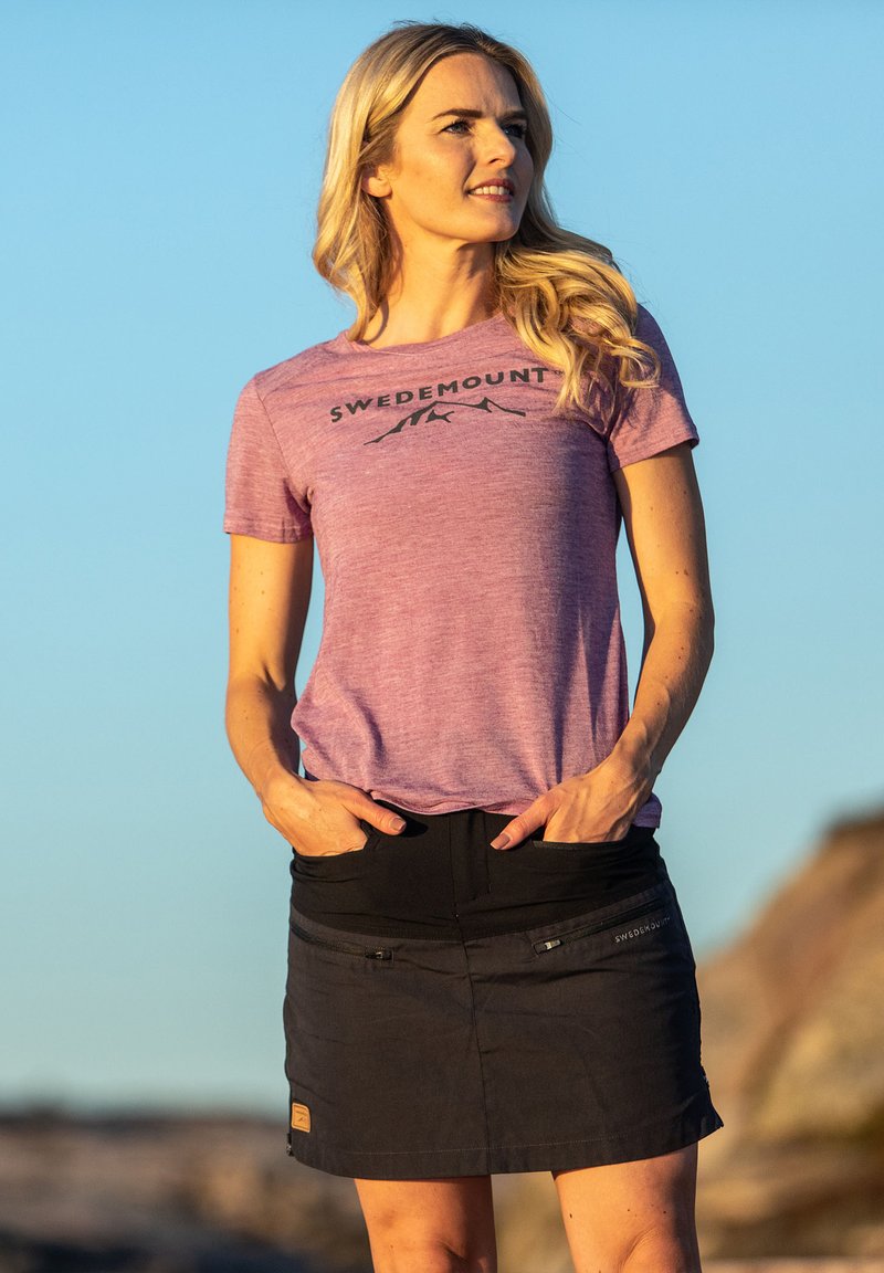 T-shirt sportivo viola con logo "SWEDEMOUNT" e skort aderente nera con tasche con zip e tessuto testurizzato.