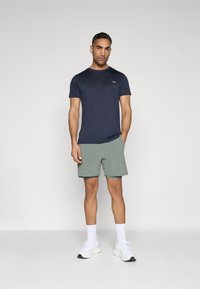Marineblå kortærmet t-shirt parret med lysegrønne shorts. Blandingsstof i bomuld, afslappet pasform, logodetalje på brystet, stylet med hvide sneakers.