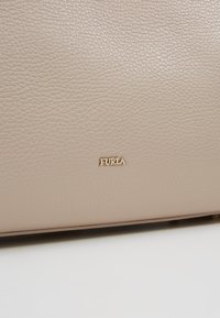 Surface en cuir beige texturé avec petit nom de marque Furla doré centré près du bord inférieur.
