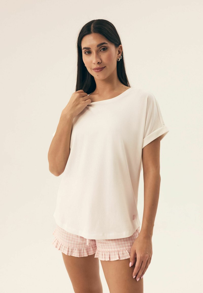 Biała, krótko rękawowa koszulka z podwiniętymi mankietami, luźny krój, gładka tekstura, w połączeniu z różowymi szortami piżamowymi w kratkę z falbaną na dole.