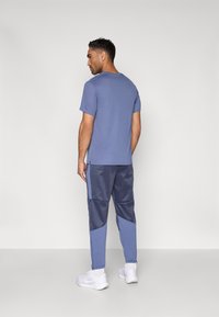 Μπλε βαμβακερό μπλουζάκι και ναυτικά παντελόνια φόρμας με αντίθετα ανοιχτά μπλε πάνελ, με άνετη εφαρμογή και μανσέτες στους αστραγάλους. Λευκά αθλητικά παπούτσια ολοκληρώνουν την εμφάνιση.