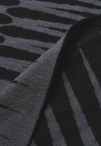 Gros plan sur un tapis gris foncé plié avec des motifs texturés verticaux et circulaires noirs.