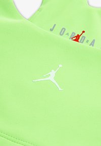 Neona zaļa sporta tops ar teksturētu audumu, ar baltu Jumpman logo un "JORDAN" sarkanā krāsā. Apaļa kakla izgriezuma un bez piedurknēm.