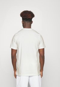 Camiseta blanca de algodón con mangas cortas y escote redondo, vista desde atrás. Textura suave, corte ajustado, sin patrones ni gráficos visibles.