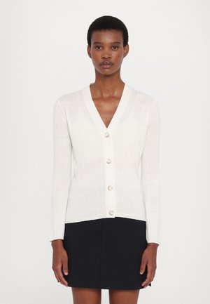 Hvit ribbestrikket cardigan med V-hals, knapp åpning og lange ermer. Laget av mykt materiale, har perle-lignende knapper og en figurtilpasset design.
