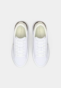 Un paio di sneakers bianche Tommy Hilfiger con lacci bianchi, dettagli beige sul tallone, viste dall'alto su uno sfondo bianco.