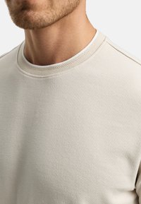 Sudadera de canalé en beige claro que presenta un escote redondo con costuras en contraste y una tela suave y texturizada.