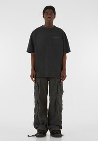 Overdimensioneret sort bomulds t-shirt med korte ærmer og et lille lilla logo på brystet, parret med mørke cargo bukser med flere lommer.