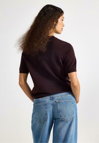 Korte mouwen, donkerbordeaux gebreide trui gecombineerd met lichtblauw denim jeans. De trui heeft een slim fit ontwerp, een gladde textuur en ribbelrandjes.