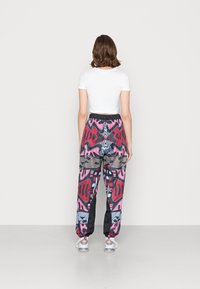 Pantalones de patrón multicolor con diseños en rosa, rojo y negro, con cintura elástica y bajos ajustados. Material de mezcla de algodón y poliéster.