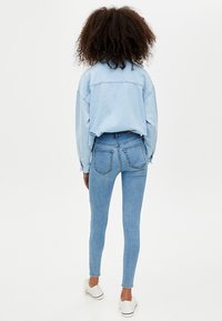 Vaqueros de mezclilla azul claro con cintura alta y silueta ajustada, combinados con una camisa de mezclilla azul de gran tamaño. Presenta bolsillos traseros y un look casual.