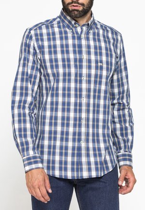 Uomo che indossa una camicia a quadri blu e bianca con bottoni e maniche lunghe e jeans blu scuro, ritagliato sotto il naso.