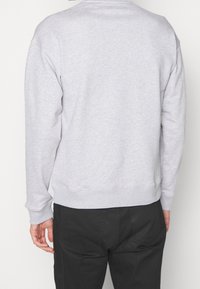 Šedá mikina s klasickým kulatým výstřihem, žebrovanými rukávy a lemem, s jemnou texturou a pohodlným střihem. Zobrazen pohled zezadu.