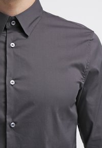 Kolgrå skjorta med klassisk krage och sex knappar fram. Slät tyg med subtil glans, skräddarsydd passform och utan mönster eller detaljer.