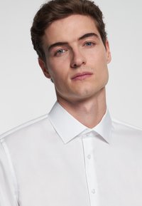 Chemise blanche à col ouvert, en tissu lisse, dotée d'une fermeture à boutons et d'un design épuré et minimaliste.