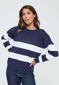 Pull rayé bleu marine et blanc avec un col rond, des poignets côtelés et des boutons décoratifs sur les épaules. Texture tricot douce.