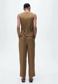 Haut en tissu marron avec un détail de nœud à la taille, associé à un pantalon large assorti. Texture lisse, design minimaliste, sans motifs visibles.