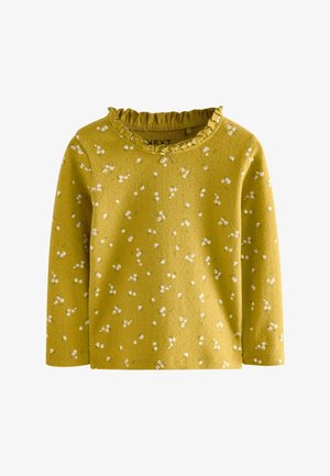 Top de manga larga en color mostaza con un cuello con volantes, que presenta patrones florales blancos dispersos. Textura suave y diseño informal.