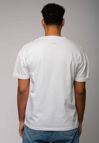 Weißes Baumwoll-T-Shirt mit kurzen Ärmeln und umgeschlagenen Ärmelabschlüssen, versehen mit einem kleinen grünen Logo auf der Mitte des Rückens. Klassische Passform mit glatter Textur.