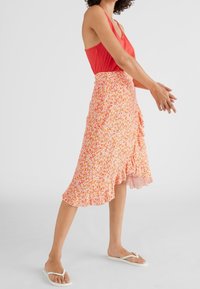 Bloemen midi rok in oranje en wit, met een gerimpelde zoom, gemaakt van lichte stof. Gecombineerd met een rode tanktop en witte teenslippers.