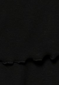 Svart ribbad tyg med en texturerad yta och scallopdetaljer i nederkant. Materialet verkar mjukt och elastiskt.