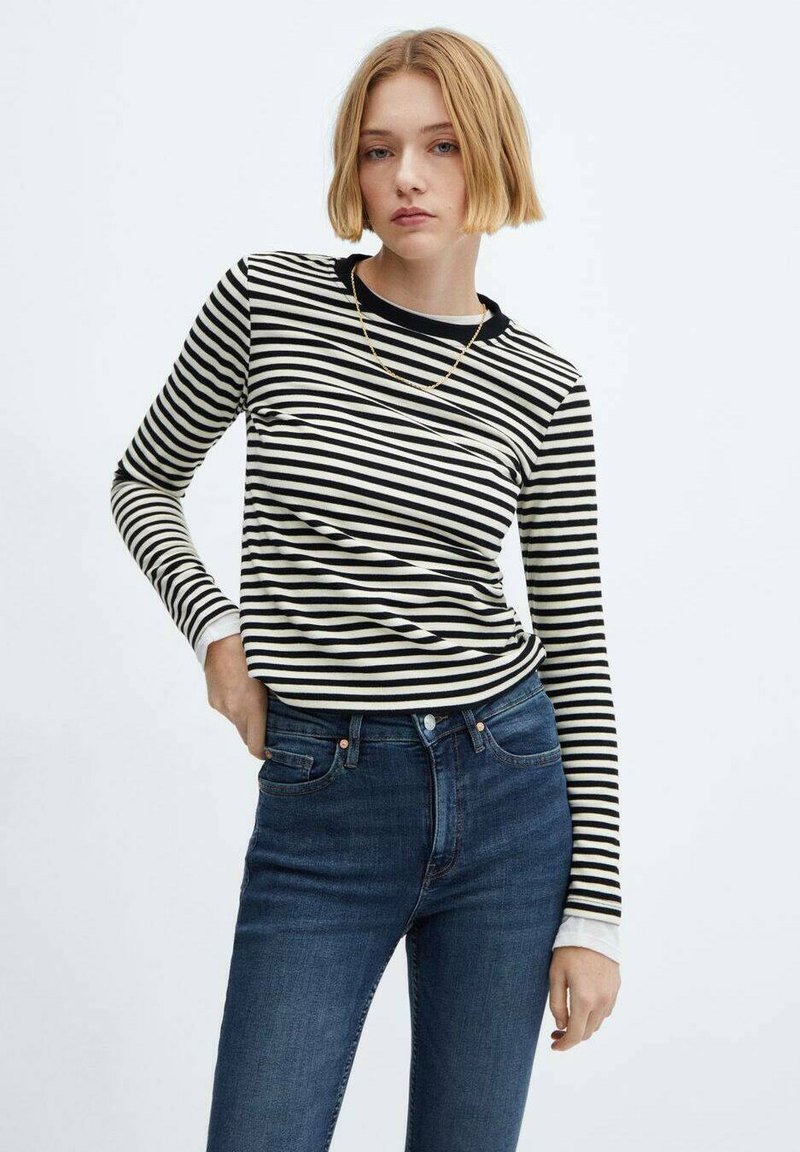 Schwarz-creme gestreiftes Langarmoberteil mit rundem Ausschnitt, kombiniert mit dunkelblauen, eng anliegenden Jeans. Weicher Stoff mit klassischer Passform.