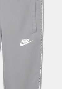 Grey Nike joggers with side pockets, white Nike logo on thigh, and white tape with repeated logos along the outer seam.