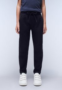 Sorte sweatpants lavet af blødt stof, med elastisk talje og snøre, sidelommer og smalle manchetter. Båret med hvide sneakers.