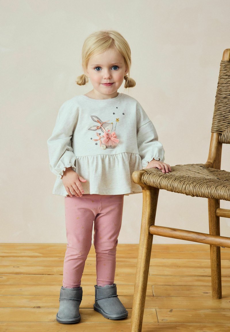 Gray peplum top with bunny embroidery, pink leggings with gold stars, and gray ankle boots, paired with a wooden chair on a wooden floor.