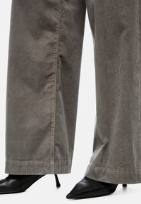 Corduroy wide-leg pants in gray, featuring vertical ribbing and a hem that tapers slightly. Paired with pointed black stiletto heels.