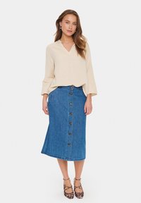 Top beige con scollo a V e maniche lunghe abbinato a una gonna di jeans blu con chiusura a bottoni. Indossato con tacchi alti di pelle maculata marrone.