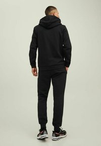 Schwarzer Hoodie mit großer Rückentasche, kombiniert mit passenden Hosen. Glatter Stoff, lässige Passform sowie elastische Bündchen und einen elastischen Bund.
