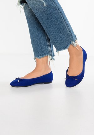 Modré semišové baleríny s kulatou špičkou, zdobené malou mašlí a kovovými akcenty. Kombinované s oholenými džínovými zkrácenými kalhotami.