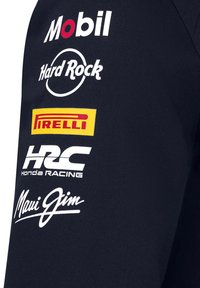 Rękaw marynarskiej kurtki drużynowej z białymi logotypami sponsorów: Mobil, Hard Rock, Pirelli, HRC Honda Racing i Maui Jim. Teksturowana tkanina.