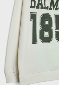Felpa color crema con grande testo verde e il numero "185" in un carattere audace. I polsini sono elasticizzati e testurizzati.