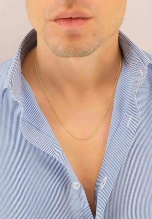 Primo piano del volto inferiore e del collo di un uomo che indossa una sottile collana d'oro e una camicia a righe blu e bianche con colletto aperto.