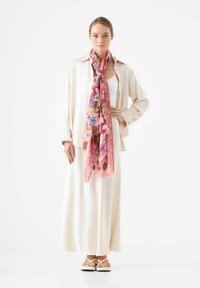 Lichtgewicht roze sjaal met bloemenpatronen, gedragen over een crèmekleurig blouse en een lange rok. Enkele sandalen maken de look compleet.