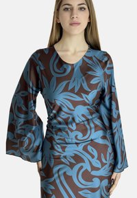 Robe à manches longues en satin marron avec des motifs floraux et enroulés bleus, dotée d'un décolleté arrondi et d'une silhouette ajustée.