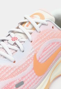 Αθλητικά παπούτσια Nike με ροζ και λευκό διαβαθμισμένο πλεκτό πάνω μέρος, πορτοκαλί λογότυπο Swoosh και λευκά κορδόνια με μικρή κόκκινη floral διακοσμητική λεπτομέρεια.