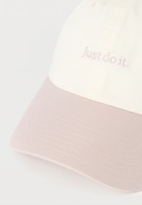 Bawełniana czapka z daszkiem w kremowym kolorze z różowym, teksturowanym daszkiem, z haftowanym napisem "Just do it." w dopasowanym różowym kolorze na przodzie.