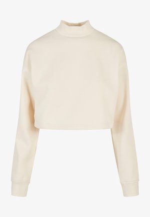 Krótkia bluza w kolorze kremowym, z długimi rękawami, wysokim dekoltem i miękką fakturą z prążkowanymi akcentami przy kołnierzu i mankietach.