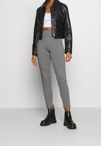 Zwarte neplederen jacket met een cropped ontwerp, gecombineerd met strakke zwart-wit houndstooth leggings en zwarte enkellaarsjes.