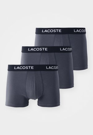 Tre par mørkegrå boxer shorts med en sort elastisk linning, der har brandnavnet i hvid skrift, lavet af blødt og strækbart materiale.