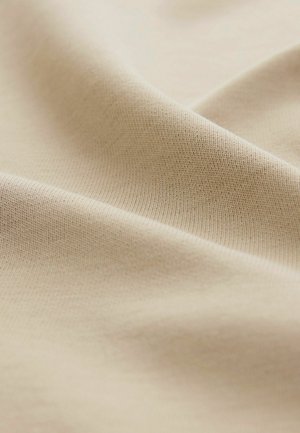 Un tessuto di cotone beige si drappeggia dolcemente, mostrando una consistenza liscia e un delicato motivo a coste, con sottili variazioni di luce e ombra.