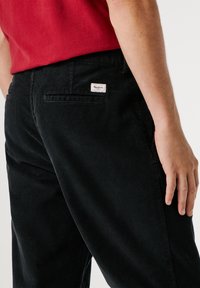 Zwarte corduroybroek met een gestructureerd oppervlak, voorzien van een achterzak en een klein label op de tailleband. Het ontwerp heeft een straight-leg pasvorm.