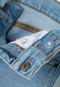 Světle modré džíny z denimu s částečně rozepnutým zipem, viditelnou bílou vnitřní látkovou etiketu, knoflíkem a kovovým háčkem na zapínání.